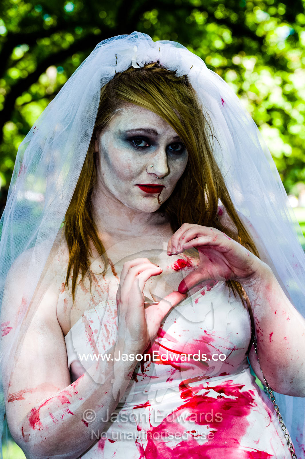 A blood-soaked zombie bride makes the heart shape with her fingers. Carlton Gardens, World Heritage Site, Carlton, Melbourne, Victoria, Australia.