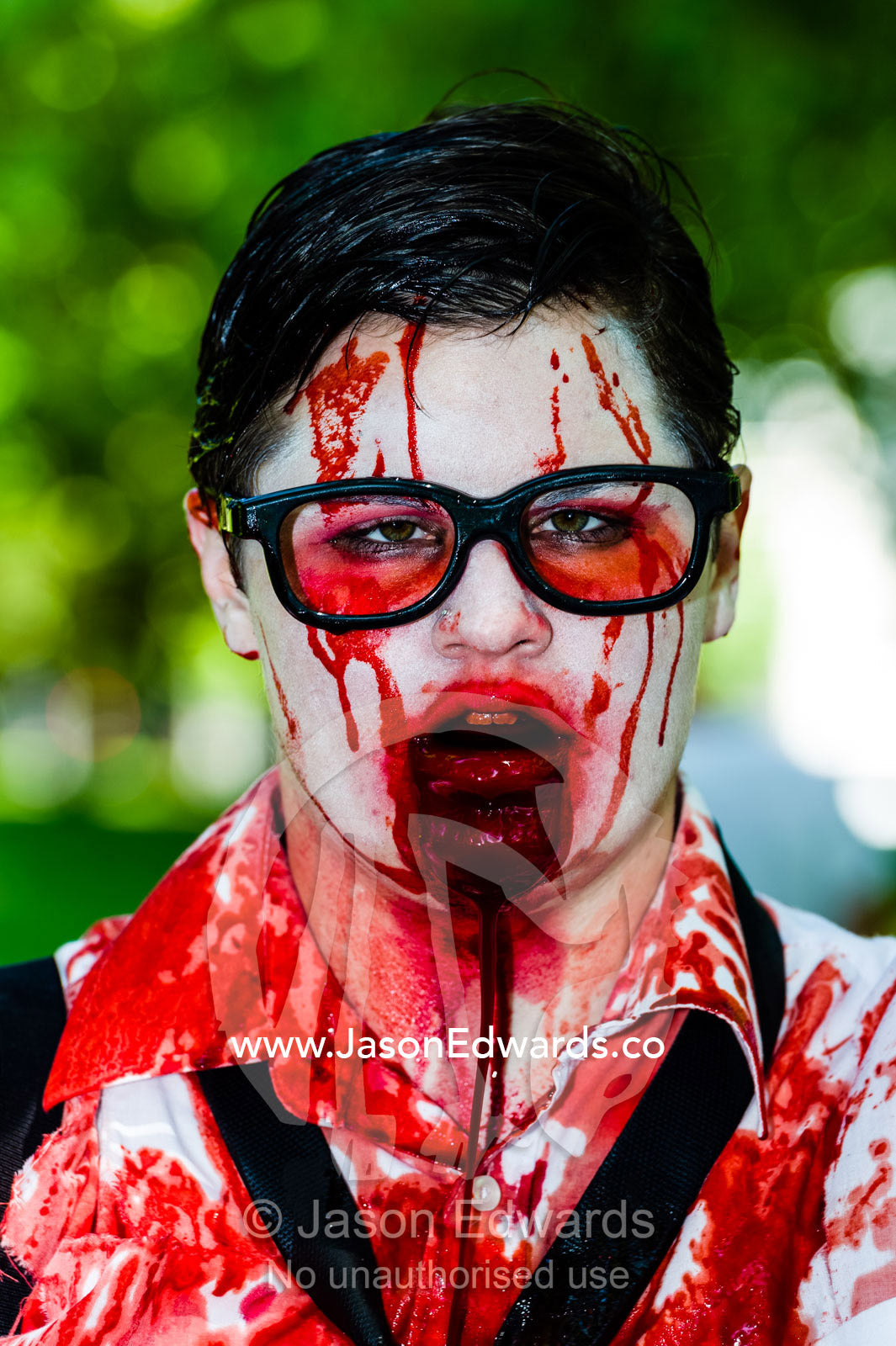 A drooling, blood-soaked zombie wearing glasses at a festival. Carlton Gardens, World Heritage Site, Carlton, Melbourne, Victoria, Australia.