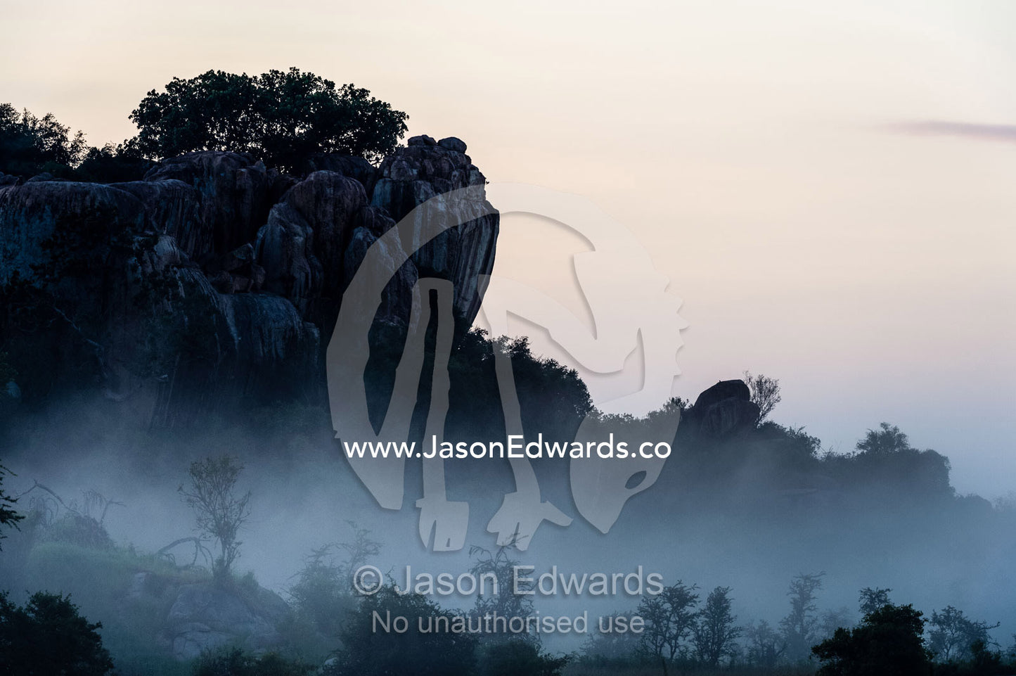 In a cold pre-dawn mist and fog surround the base of a rocky granite outcrop known as a kopje. Moru Kopjes, Serengeti National Park, Serengeti, World Heritage Site, Tanzania.