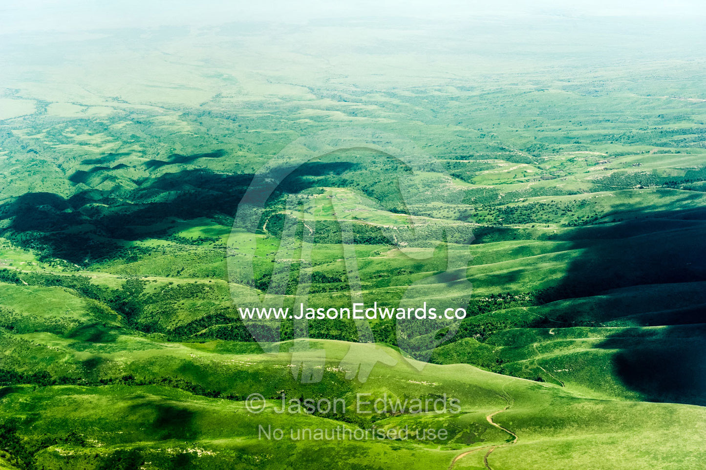 Forested volcanic mountain slopes rise above farms and the vast, green savannah plain. Crater Highlands, Ngorongoro Highlands, Serengeti National Park, Serengeti, Tanzania.