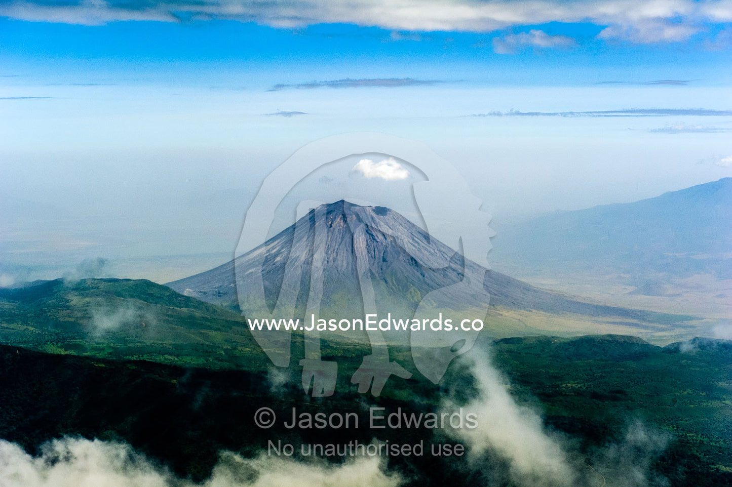 Clouds circle the summit of primeval volcano caldera shrouded in forests above the savannah plain. Crater Highlands, Ngorongoro Highlands, Serengeti National Park, Serengeti, Tanzania.