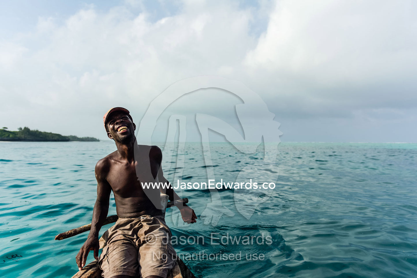A smiling fisherman steers his wooden trimaran sailing dhow in the Indian Ocean. Bwejuu, Unguja Island, Zanzibar, Tanzania, Africa.