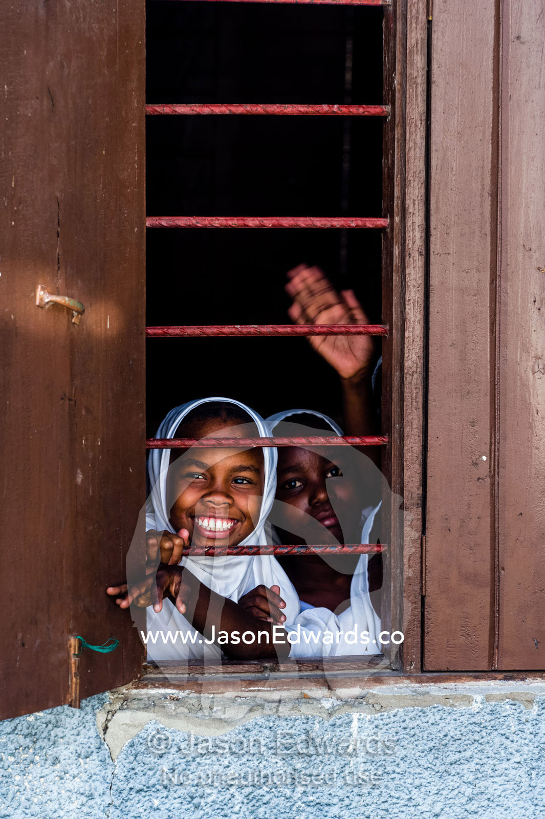 Muslim girls wave and laugh from a school classroom window. Unguja Island, Zanzibar, Tanzania, Africa.