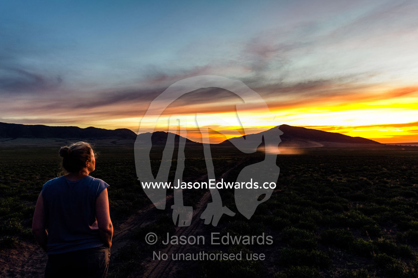 A tourist on an African safari watches a blazing sunset over distant mountains. Ngorongoro Conservation Area, Ngorongoro District, Tanzania.