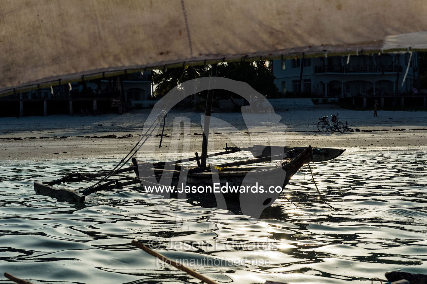 A small wooden fishing dhow moored in the shallows of a tropical island at sunset. Bwejuu, Unguja Island, Zanzibar, Tanzania.