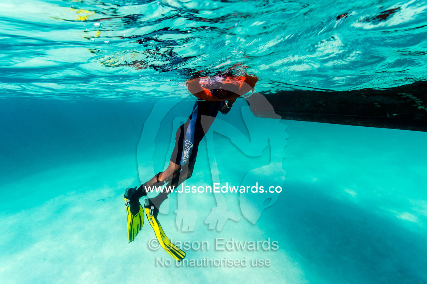An African scuba diving master floating in the water beside a dive boat. Bwejuu, Blue Lagoon Reef, Unguja Island, Zanzibar, Tanzania.