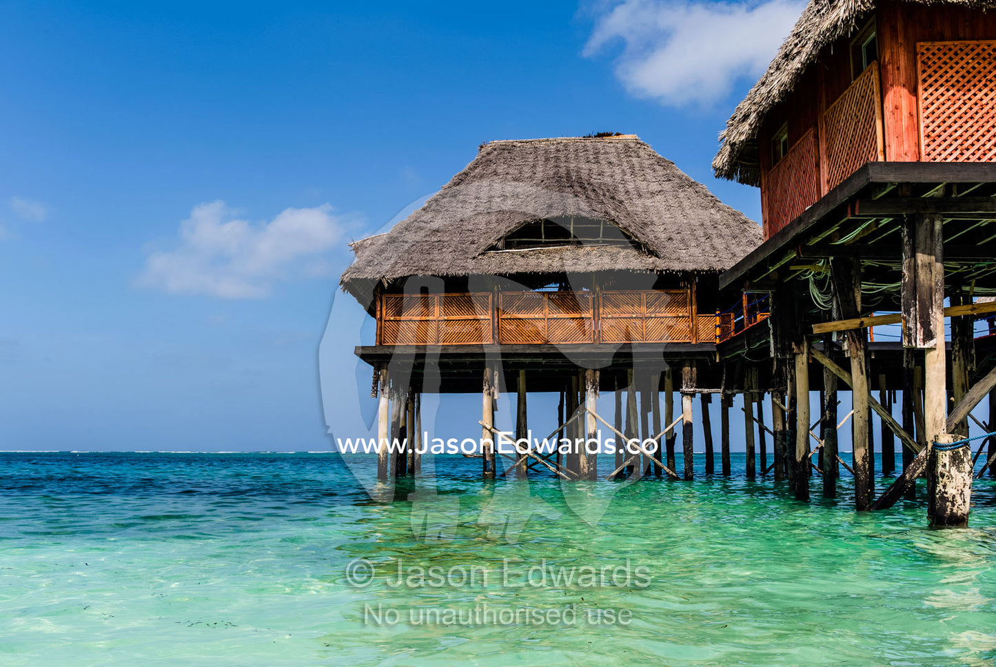 Thatched huts on stilts overlooking the turquoise waters of the Indian Ocean. Bwejuu, Blue Lagoon Reef, Unguja Island, Zanzibar, Tanzania.