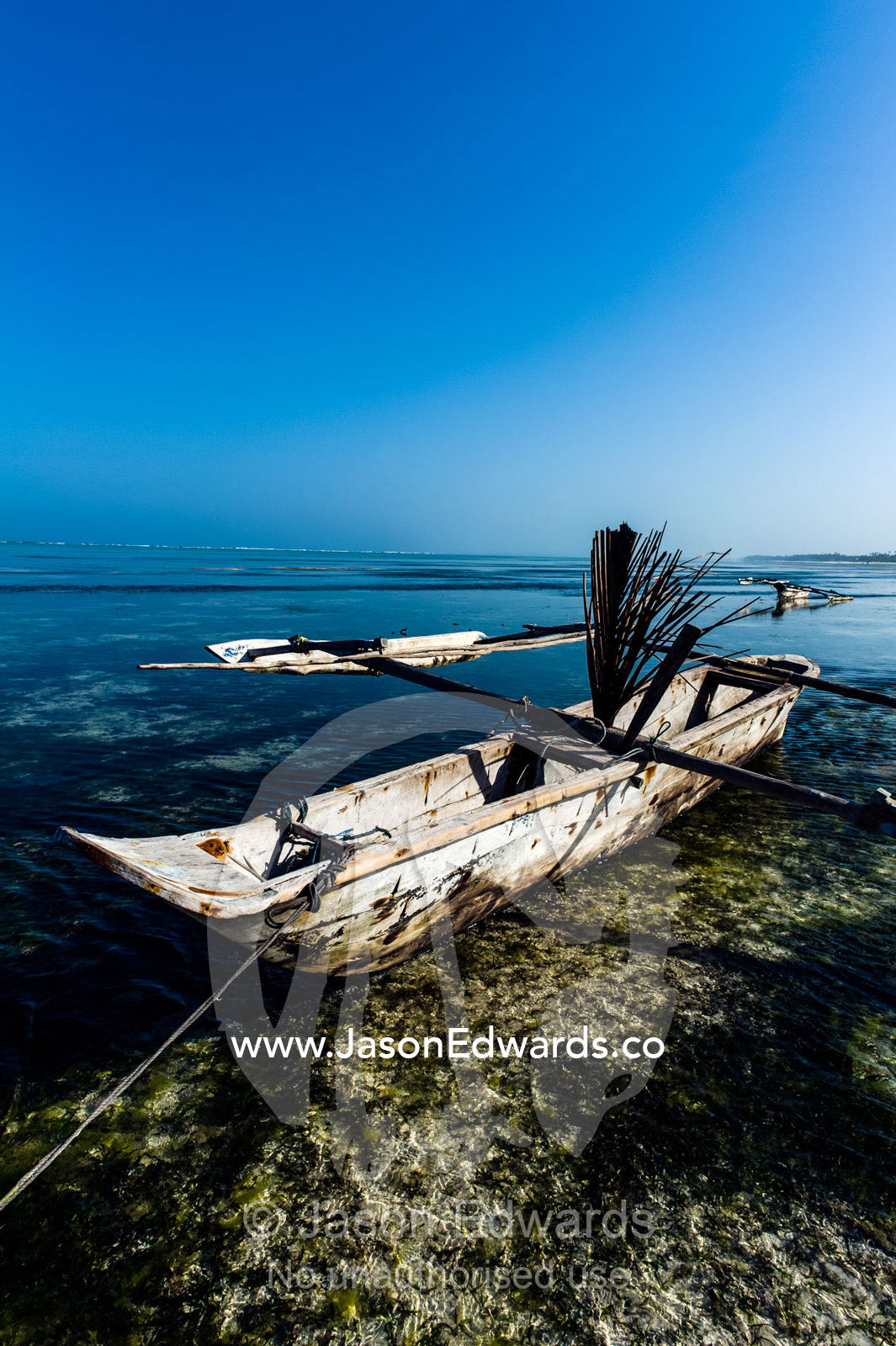A wooden trimaran fishing dhow resting in the shallows of a tropical island at low tide. Bwejuu, Echo Beach Hotel, Echo Beach, Unguja Island, Zanzibar, Tanzania.