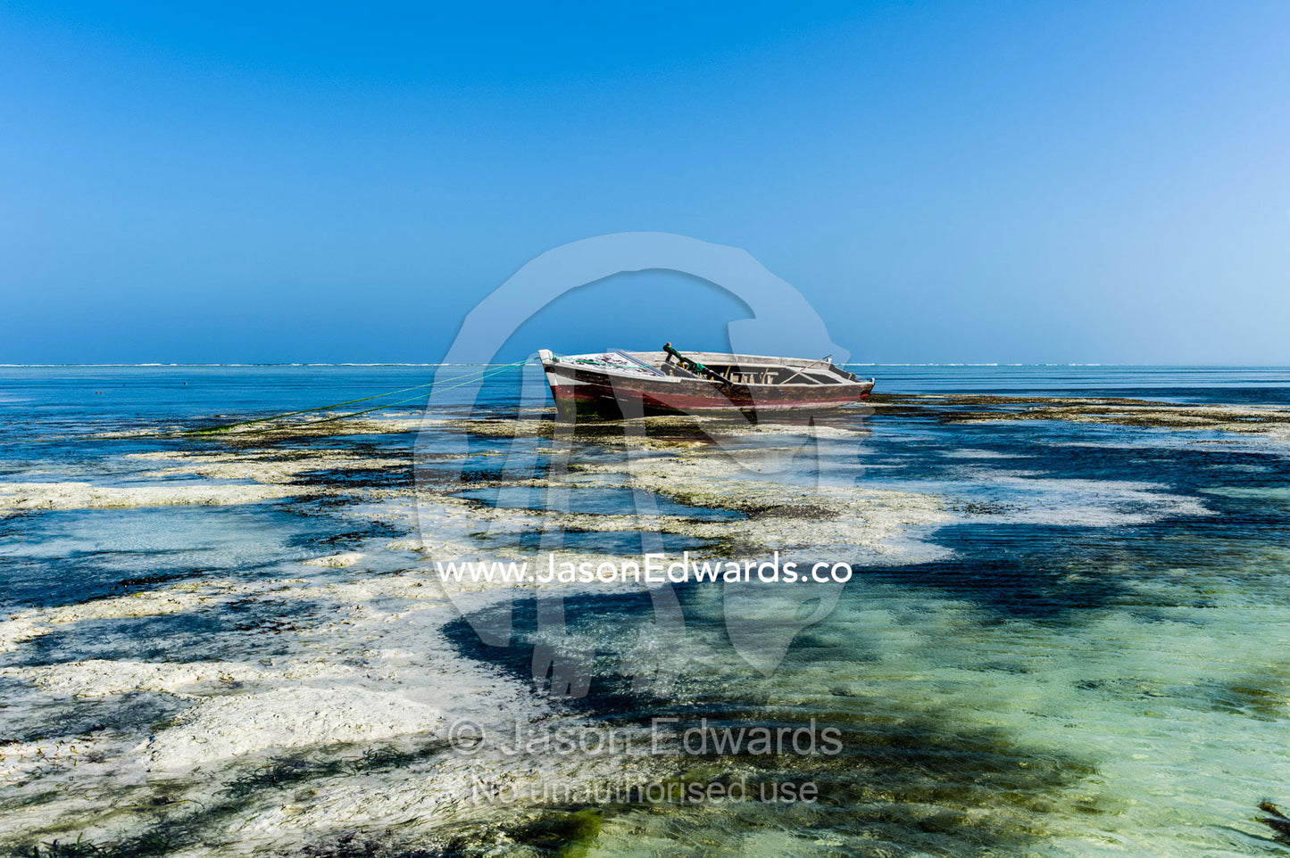 A wooden fishing boat resting in the shallows of a tropical island at low tide. Bwejuu, Echo Beach Hotel, Echo Beach, Unguja Island, Zanzibar, Tanzania.