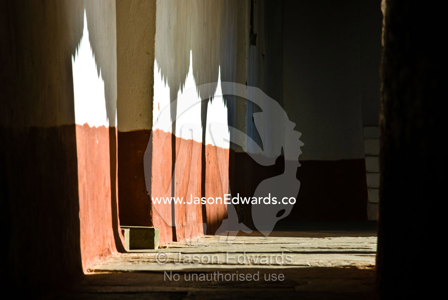 Sunlight pierces the ornate archways of a Buddhist monastery lighting a shadowed corridor. Punakha Dzong, Punakha dzongkhag, Punakha District, Bhutan.