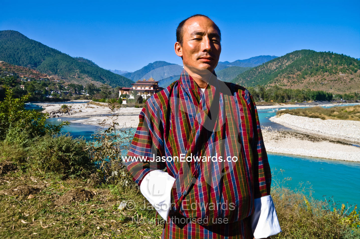 A Buddhist standing on the shore of an alpine river overlooking an ancient Buddhist monastery. Punakha Dzong, Punakha dzongkhag, Punakha District, Bhutan.