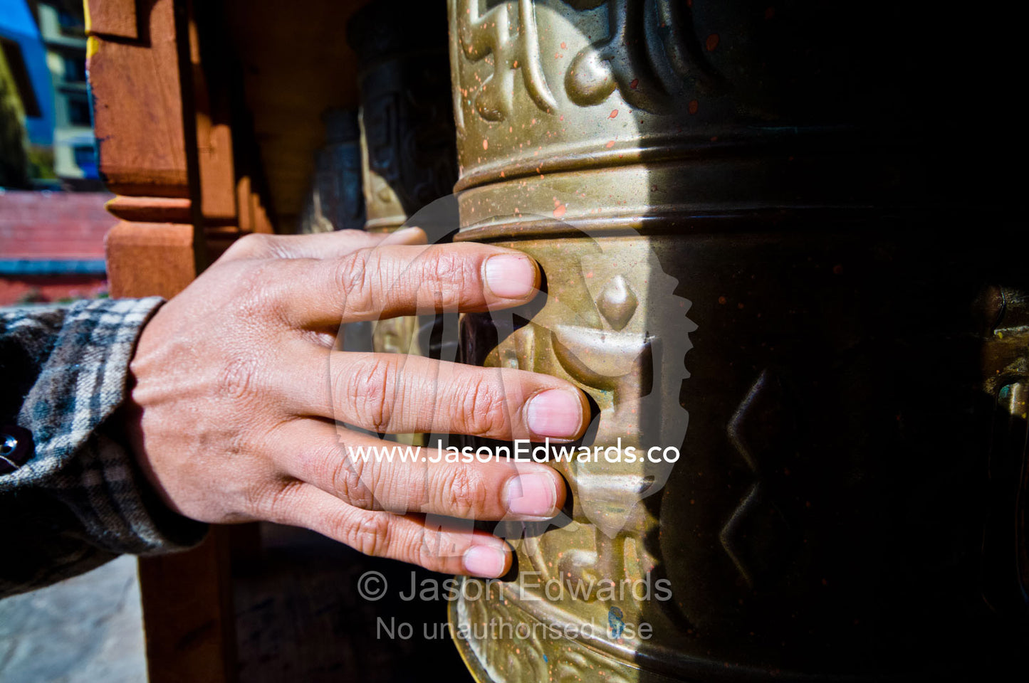 A man prepares to spin a brass prayer wheel covered in religious symbols in a Himalayan town square. Thimphu, Thimphu District, Bhutan.