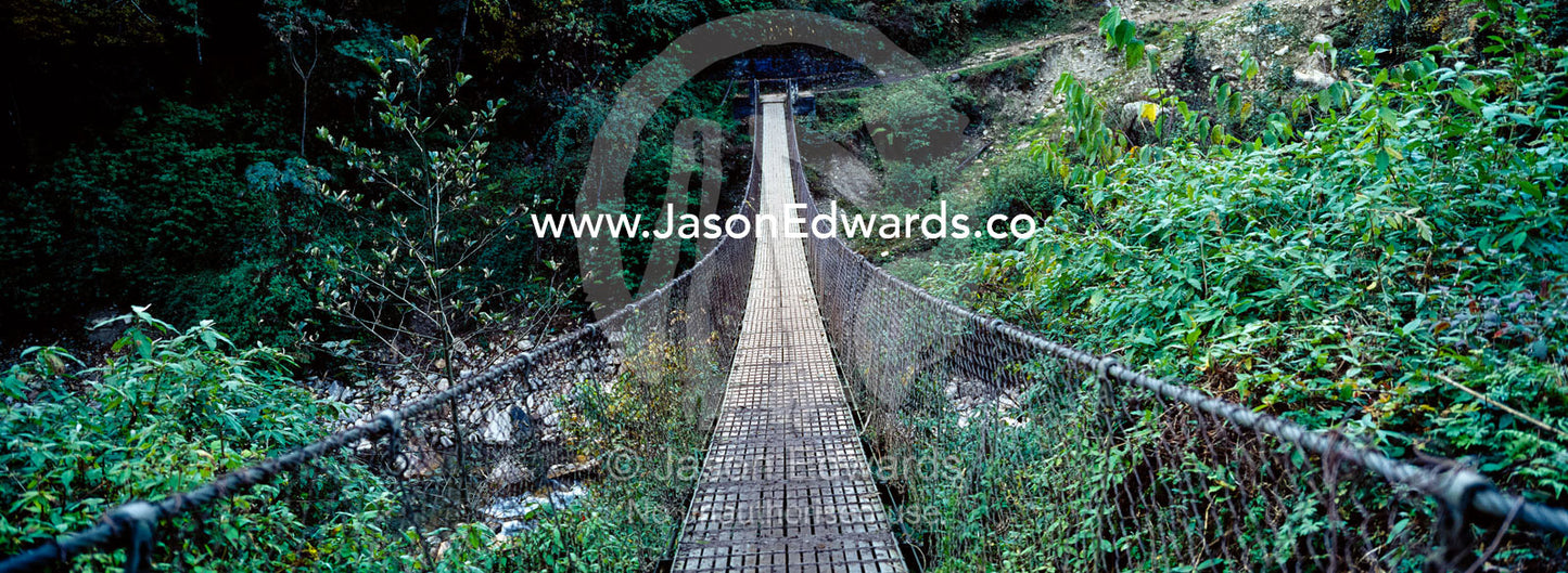 The metal planks of a suspension bridge cross between mountain valley walls in the Himalaya. Pho Chu, Pho River, Gasa, Gasa Dzongkhag District, Bhutan.