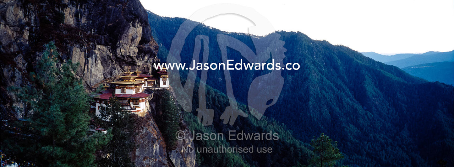 An ancient Buddhist monastery perched on a sheer cliff face above a forested valley in the Himalaya. Paro Taktsang, The Tigers Nest, Paro Valley, Paro District, Bhutan.