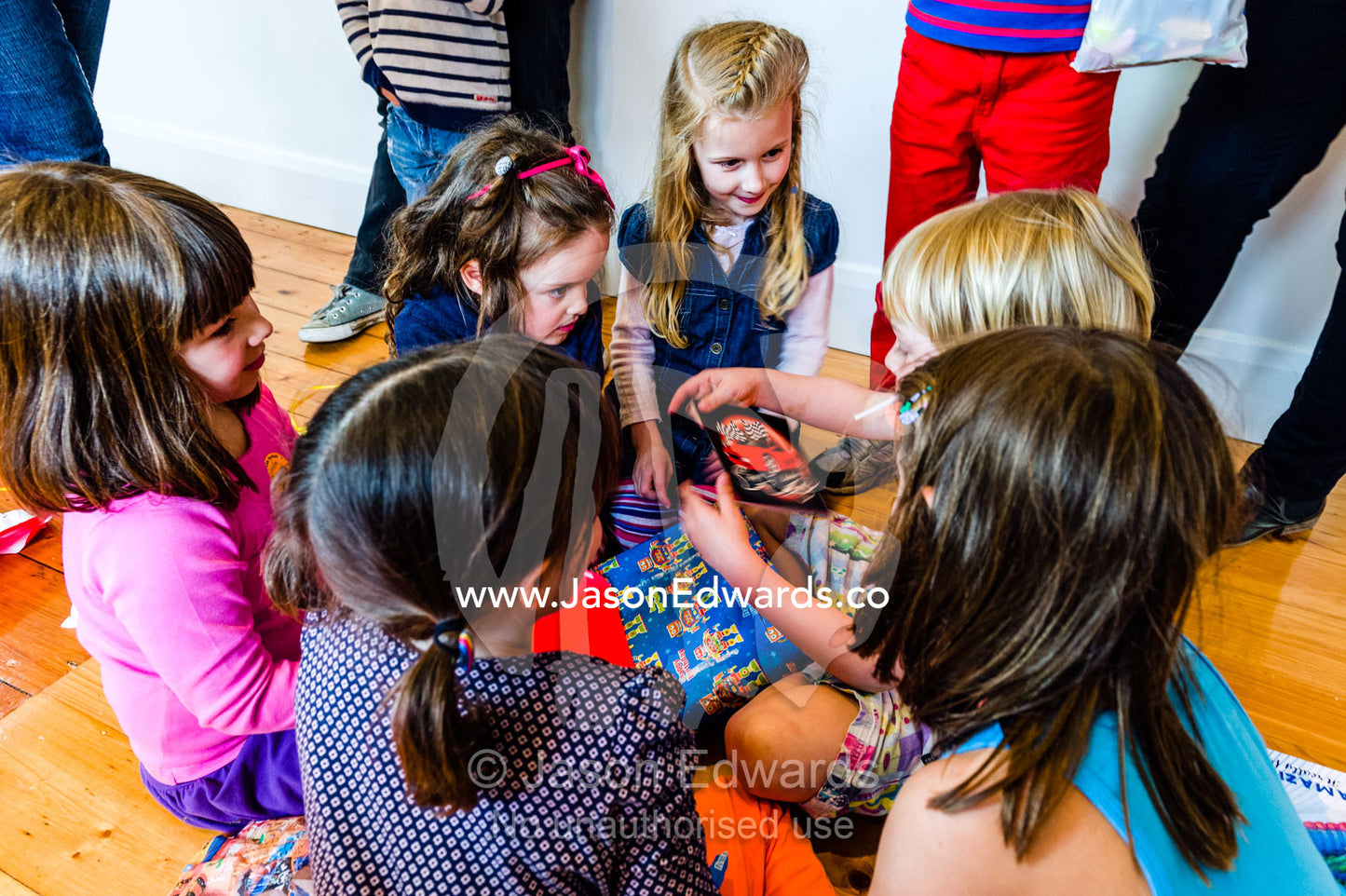 A boy opens his birthday presents surrounded by a group of girl friends. Carlton North, Melbourne, Victoria, Australia.