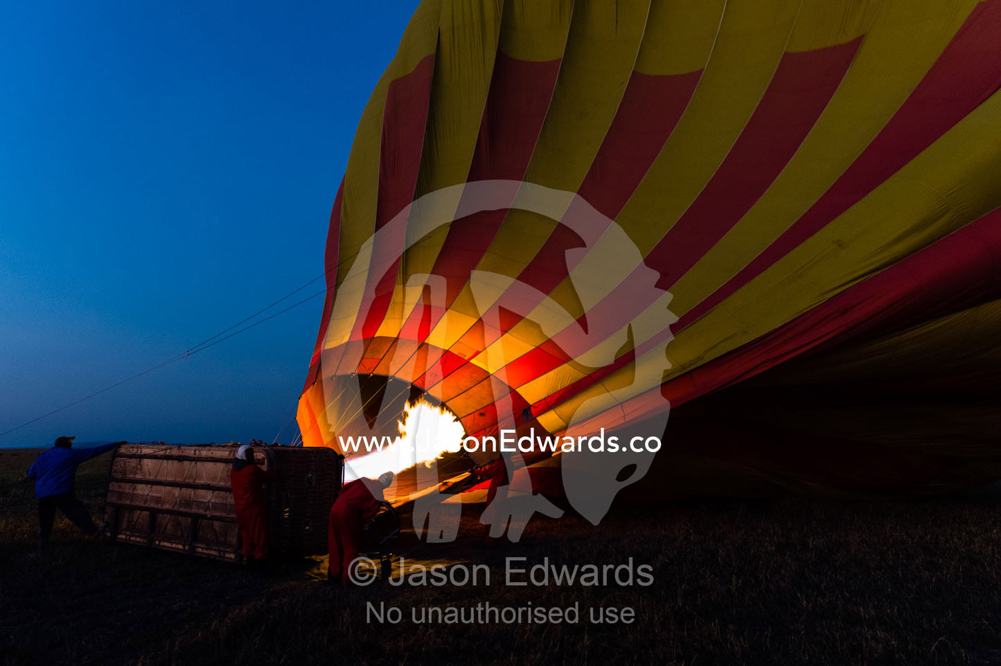 A gas jet flame fills a hot air balloon at dawn for a tourist flight over the African savannah. Maasai Mara National Reserve, Masai Mara, Narok County, Kenya.