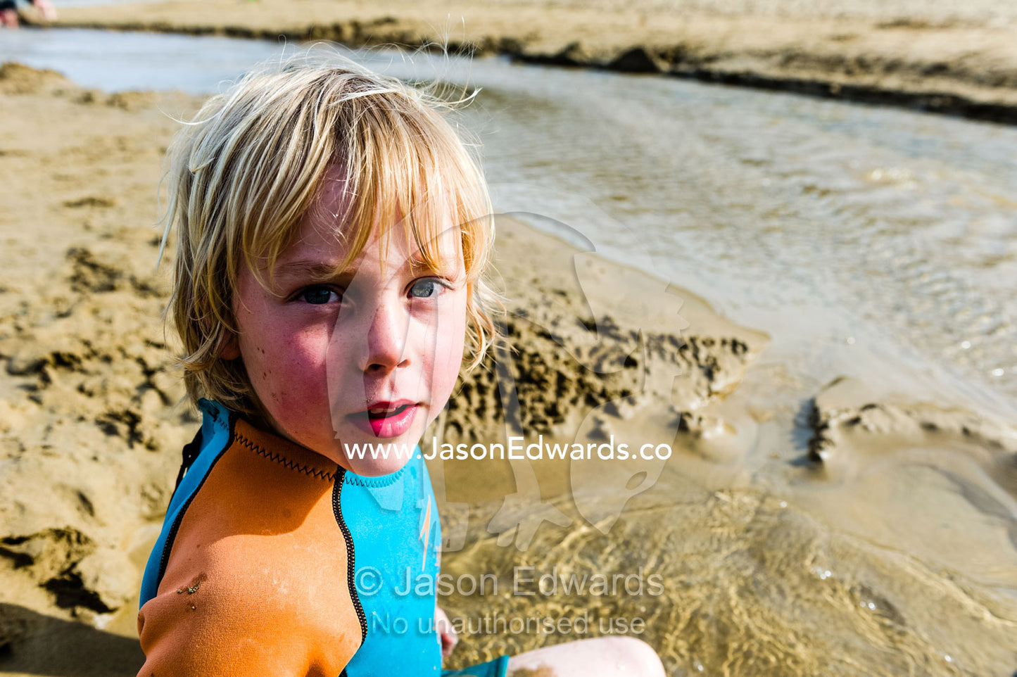 A boy playing in the sand beside a tidal stream flowing down a beach. Wye River, Great Ocean Road, Victoria, Australia.