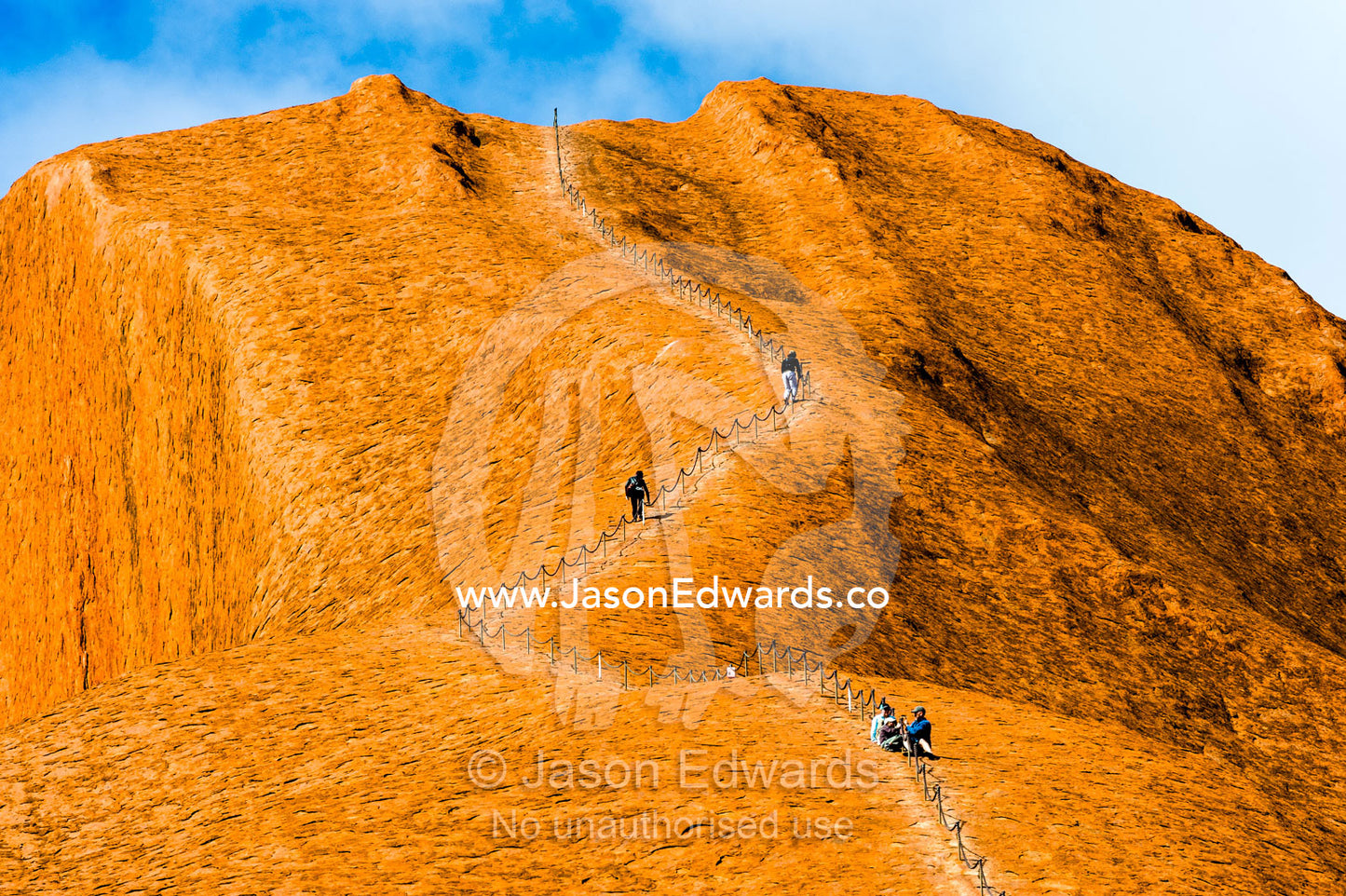 Uluru dwarfs tourists and walkers using a chain to climb its steep, smooth, oxidized slopes. Uluru Kata Tjuta National Park, Northern Territory, Australia.