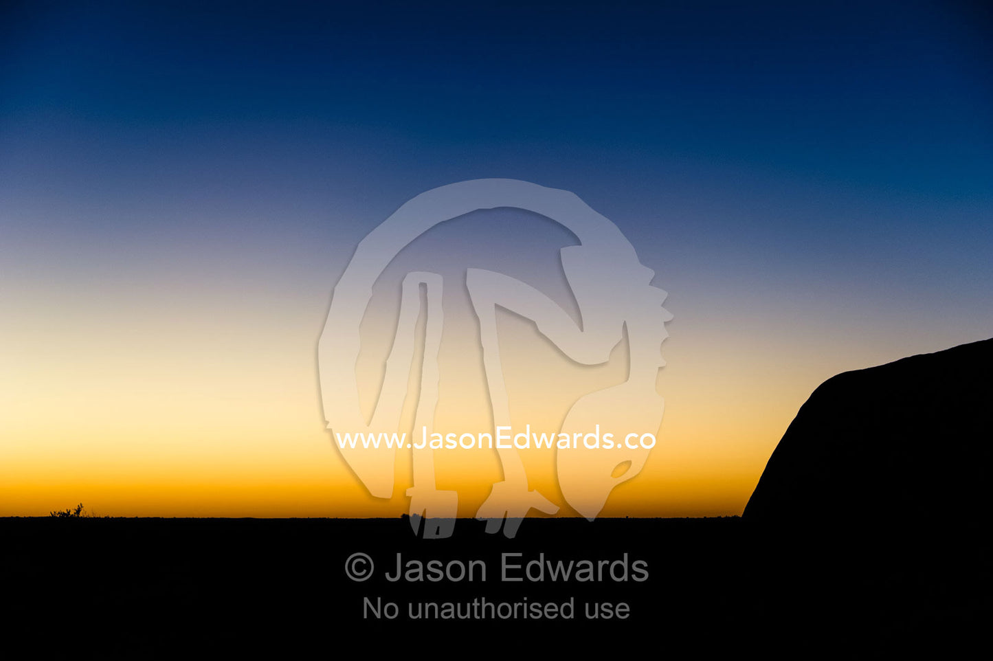 The silhouette of Uluru in the pre-dawn light on the desert plain. Uluru Kata Tjuta National Park, Northern Territory, Australia.
