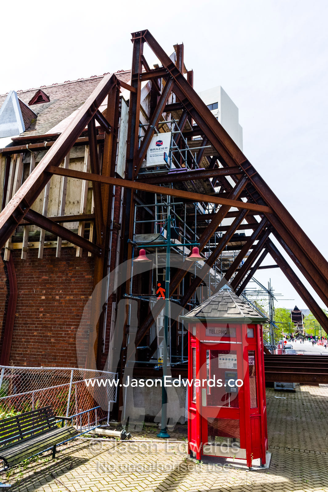 An antique English telephone box beside steel girders supporting an earthquake damaged building. Christchurch, South Island, New Zealand.