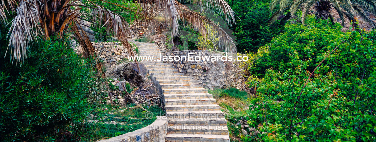 Stone steps lead up a mountain path between terrce gardens in a desert village. Wakan Village, Wadi Mastal, Wilayt Nakhal, Al Batinah South Governorate, Sultanate of Oman.