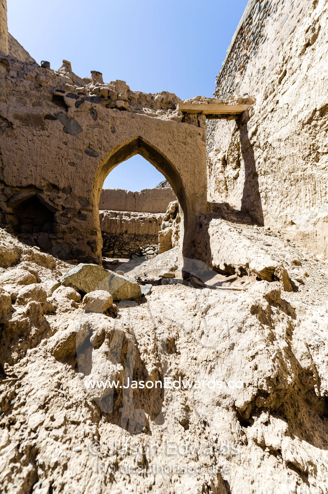 Ornate mud brick archways and doorways above rubble collapsing in an abandoned village in the desert. Ibra, Ash Sharqiyah Region, Sultanate of Oman.