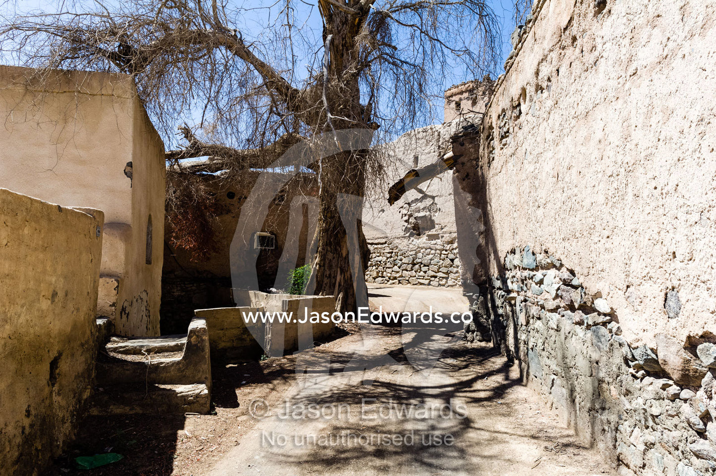 A narrow street winds it's way through an abandoned village in the desert. Ibra, Ash Sharqiyah Region, Sultanate of Oman.