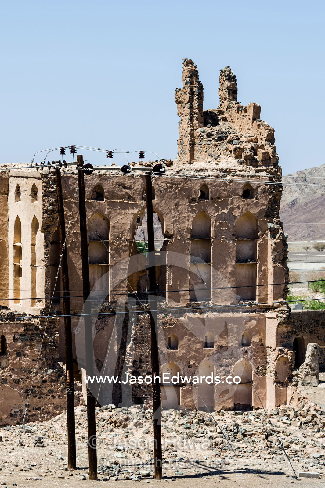 Rusting electricity poles beside an ancient crumbling ruin in a desert village. Ibra, Ash Sharqiyah Region, Sultanate of Oman.