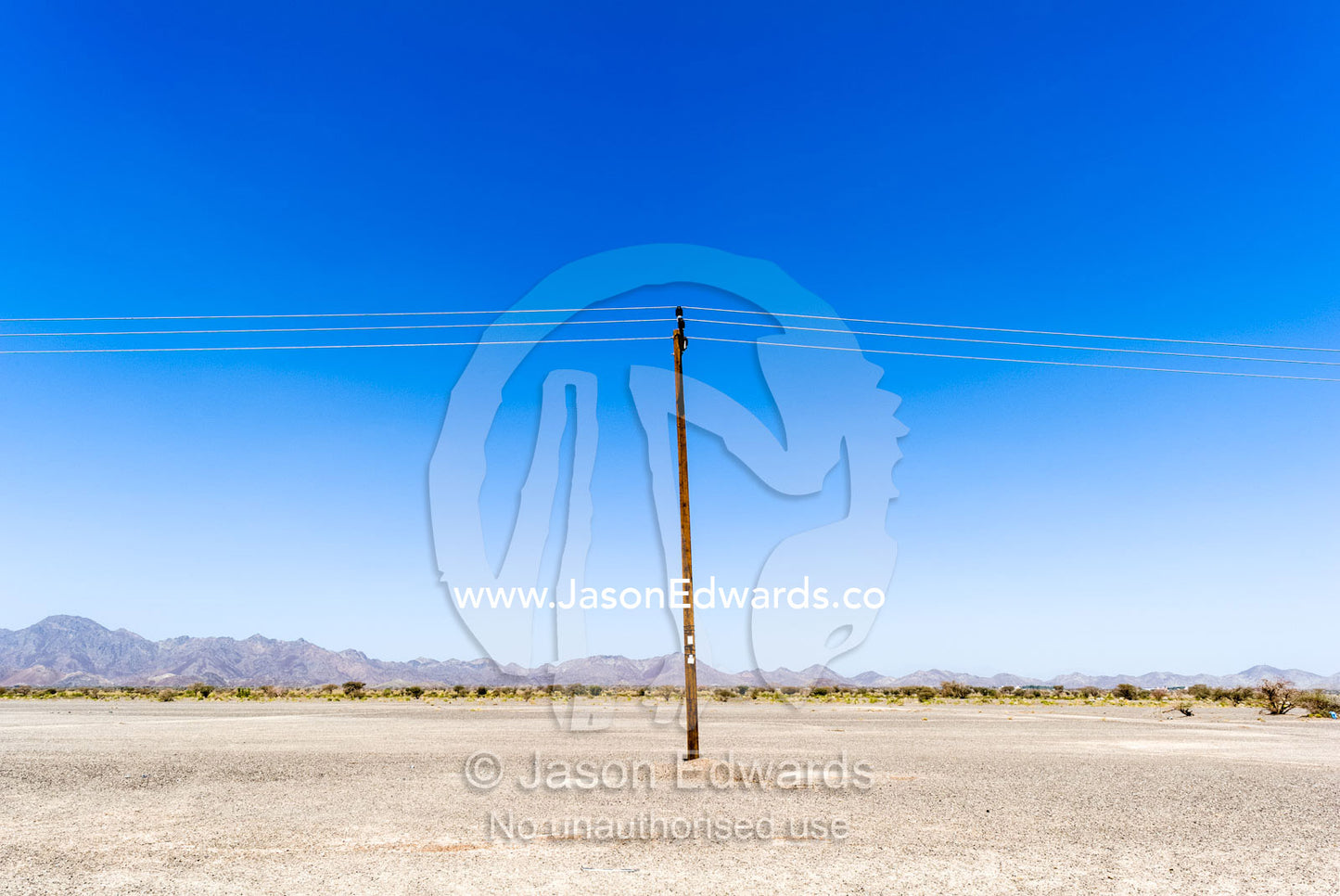 A solitary electricity pole running through a flat and barren desert. Nizwa, Sultanate of Oman.