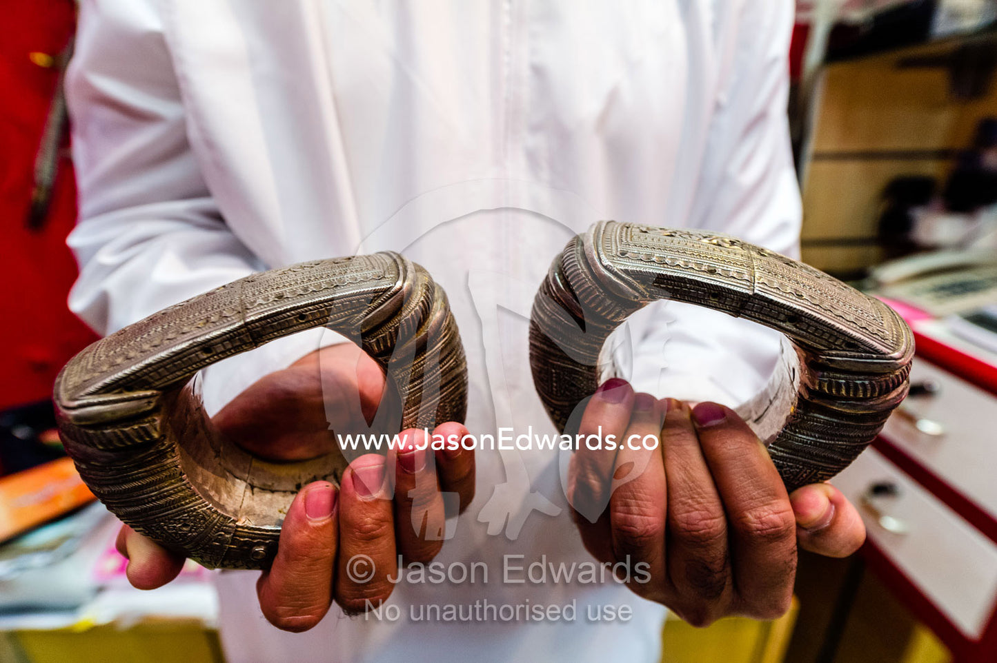 A salesman displays a pair of antique silver ankle bangles for sale in a souq. Mutrah Souq, Muscat, Sultanate of Oman.
