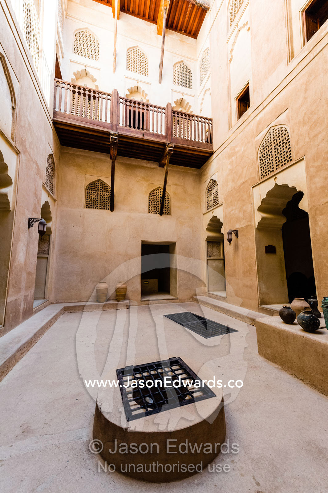 Timber balconies overlook latticed windows and a shaded well in an ancient fort courtyard. Jabrin Fort, Ad Dakhiliyah Governorate, Sultanate of Oman.