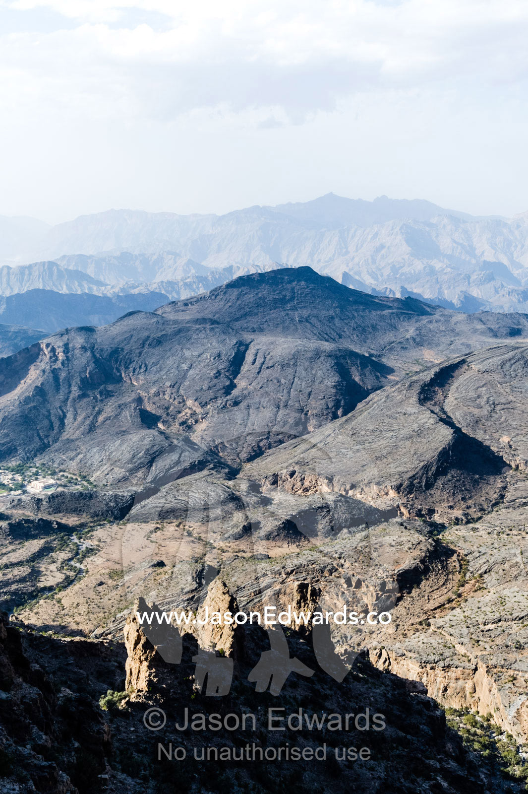 Arid jagged mountains overlook an eroded and inhospitable rocky desert valley. Hatt, Wadi Bani Awf, Snake Gorge, Western Hajar Mountains, Ad Dakhiliyah Region, Sultanate of Oman.