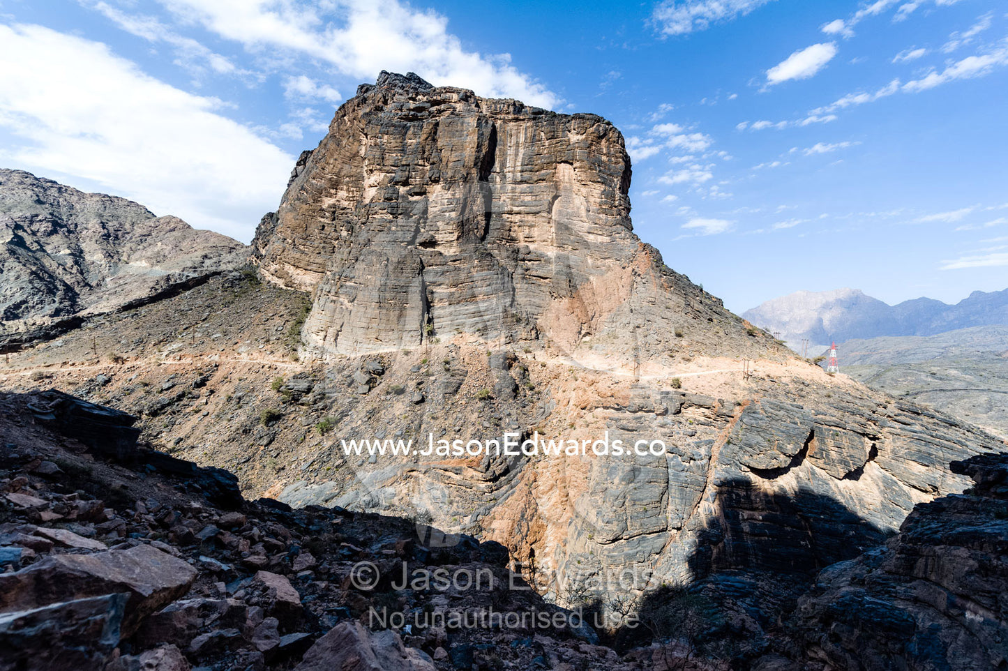 A winding dirt road dissects a steep cliff on a mountainside. Wadi Bani Awf, Snake Gorge, Western Hajar Mountains, Ad Dakhiliyah Region, Sultanate of Oman.