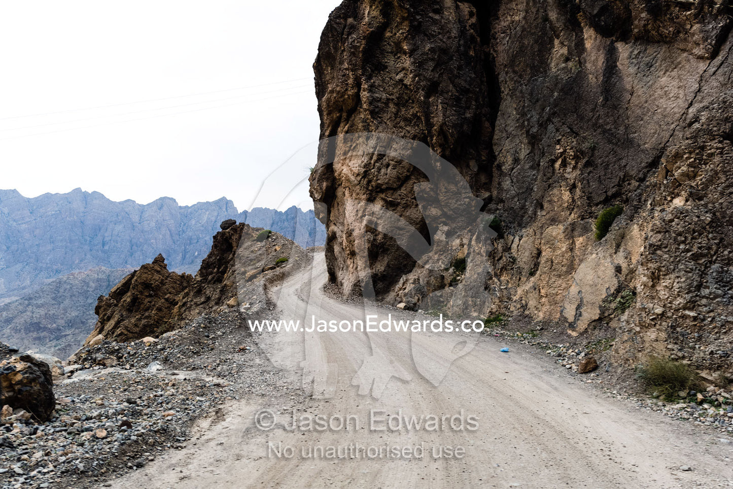 A dirt trail winds it's way through an arid desert valley. Wakan Village, Wadi Mastal, Wilayt Nakhal, Al Batinah South Governorate, Sultanate of Oman.