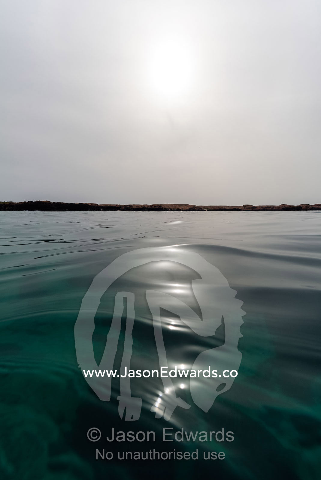 A faint sun pierces a grey sky over a calm ocean surface in the Gulf of Oman. Daymaniyat Islands Nature Reserve, Wilayat AlSeeb, Barka, Sultanate of Oman.