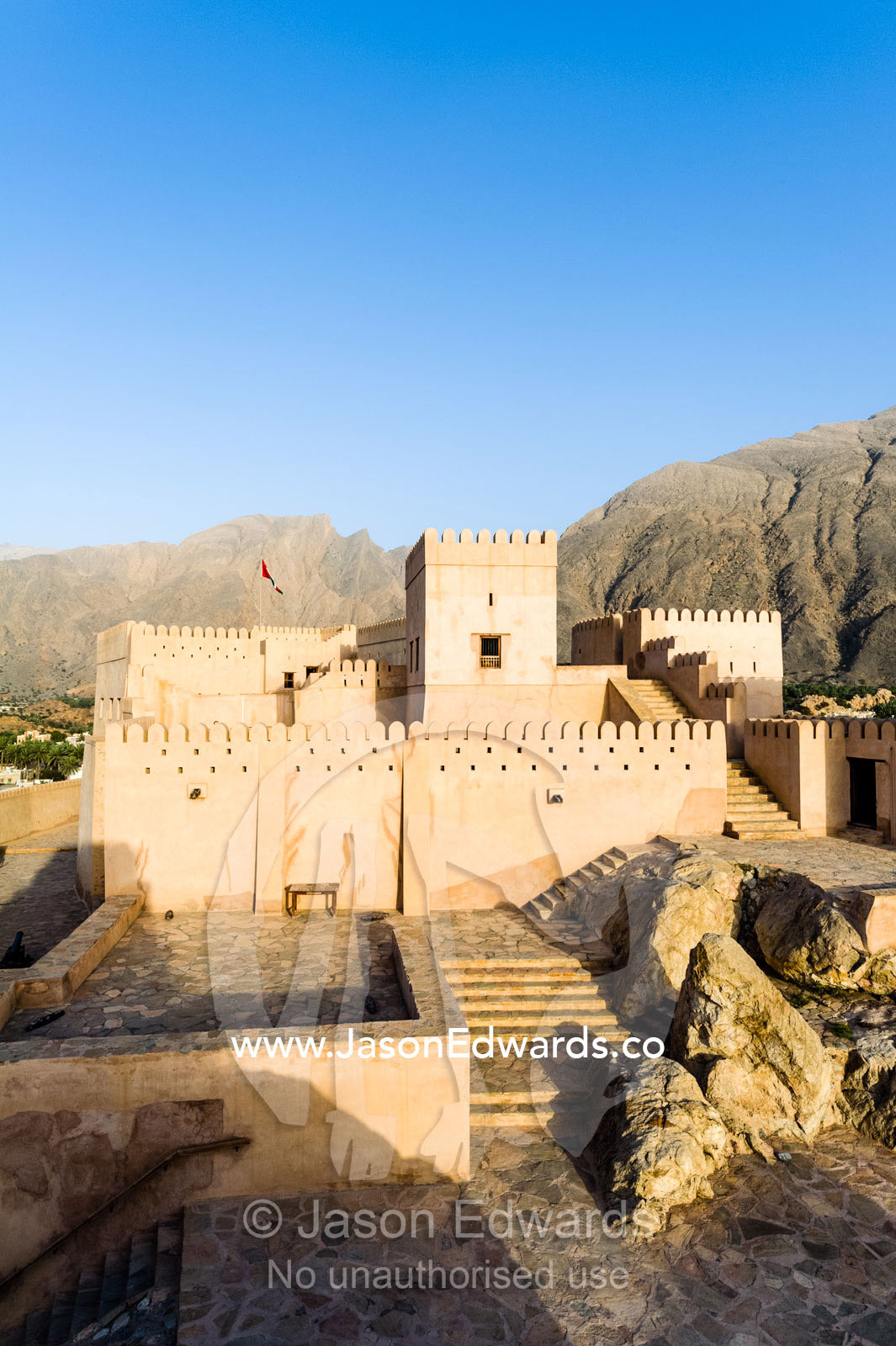 The ancient walls, parapets, battlements and watch tower of a fort on a desert mountaintop. Nakhal Fort, Wilayt Nakhal, Mount Nakhal, Al Batinah South Governorate, Sultanate of Oman.