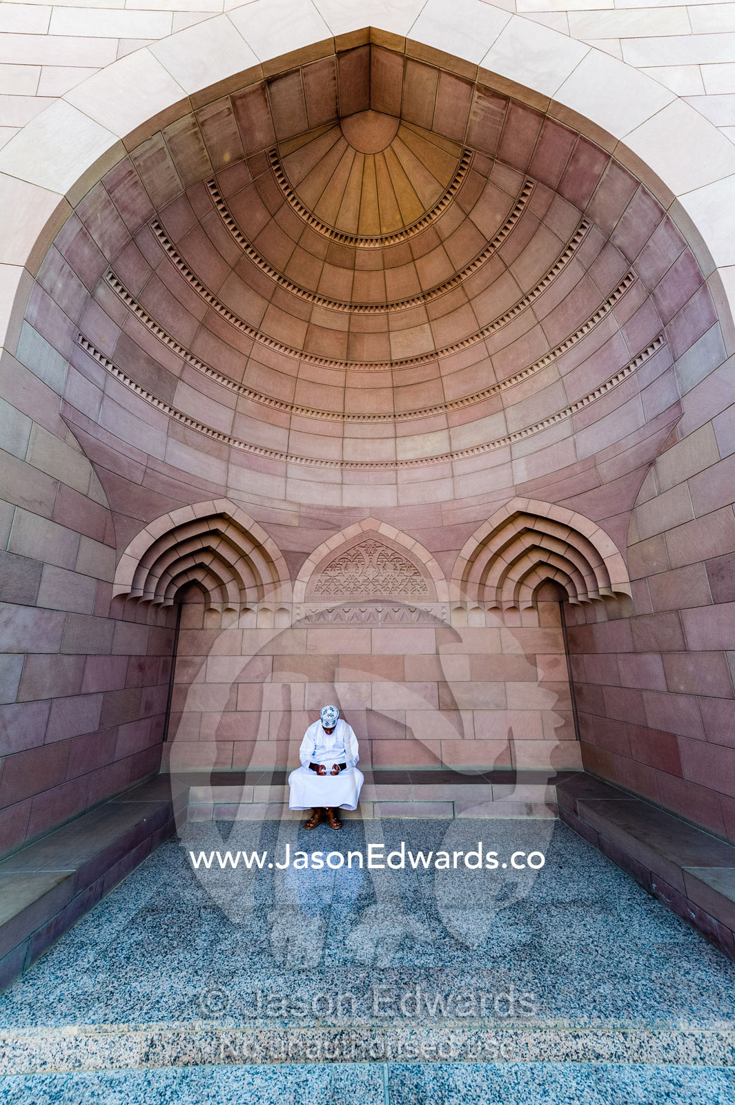 A Muslim man in a dishdasha and kuma texting on his mobile phone at the Grand Mosque. Sultan Qaboos Grand Mosque, Muscat, Sultanate of Oman.