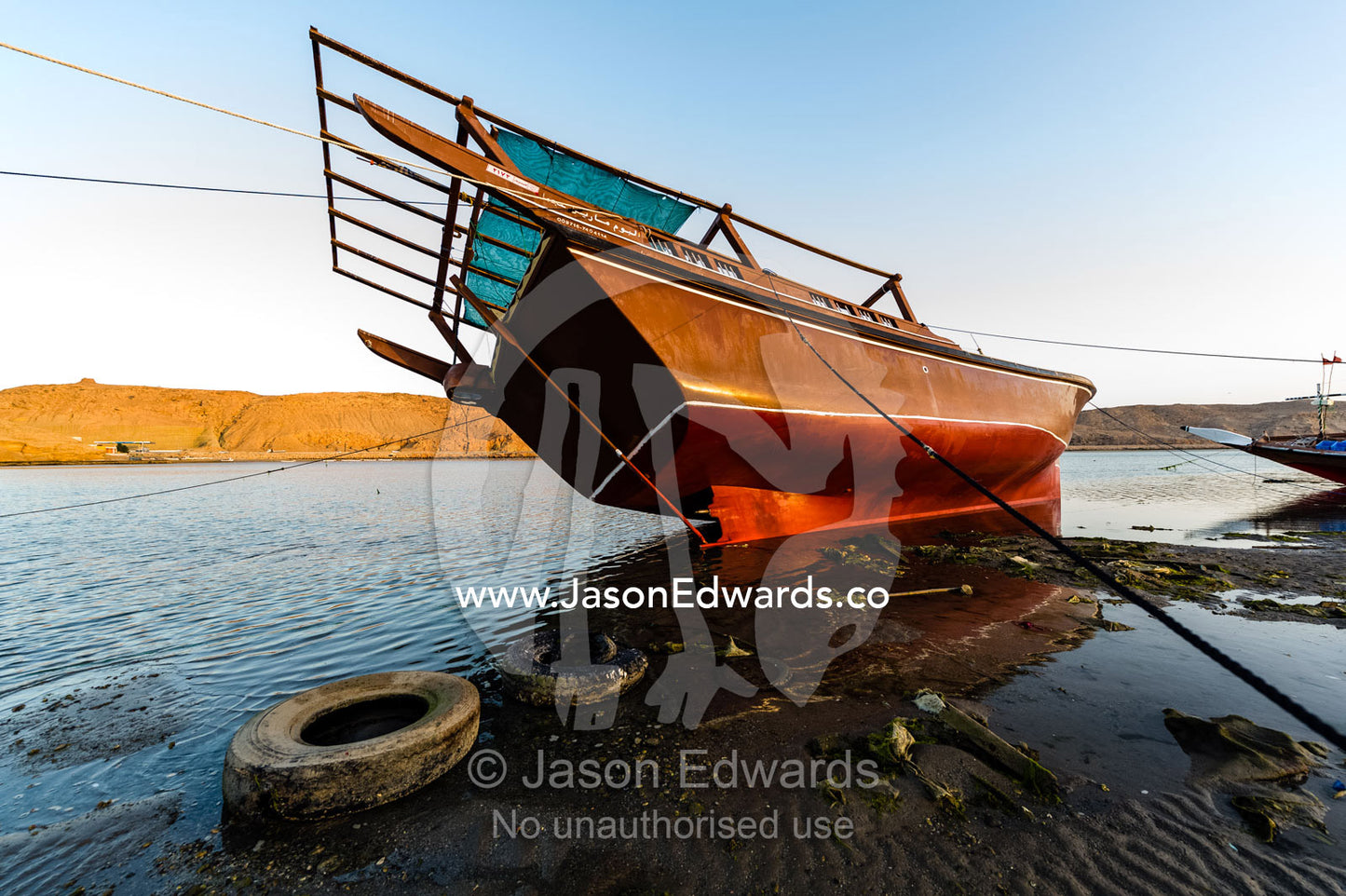 Guide ropes restrain a dhow resting in the mud on a beach at low tide. Sur, Ash Sharqiyah Region, Gulf of Oman, Sultanate of Oman.