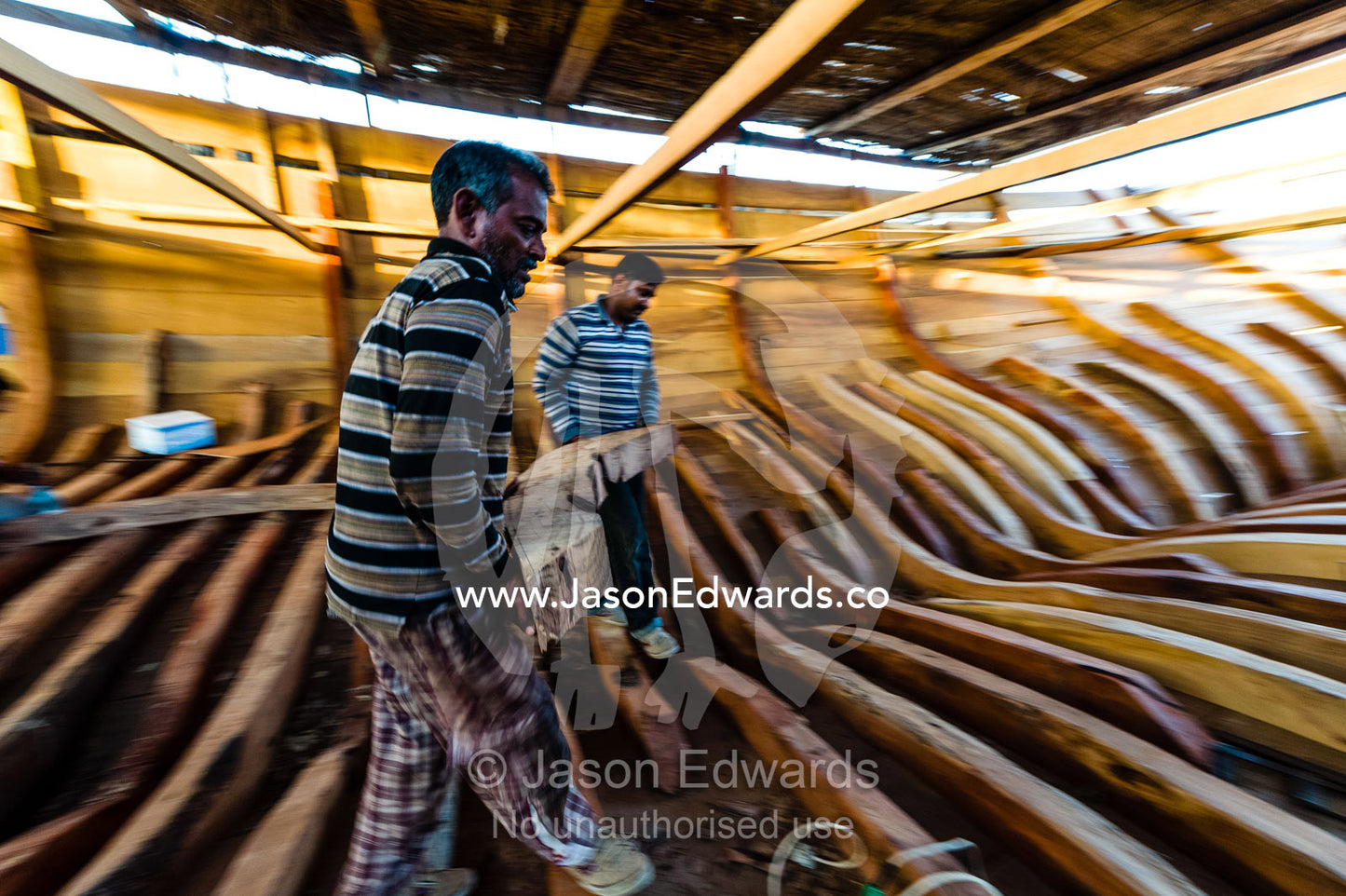 Laborers carry timber hull ribs during the handmade construction of an ancient timber dhow. Sur, Ash Sharqiyah Region, Gulf of Oman, Sultanate of Oman.