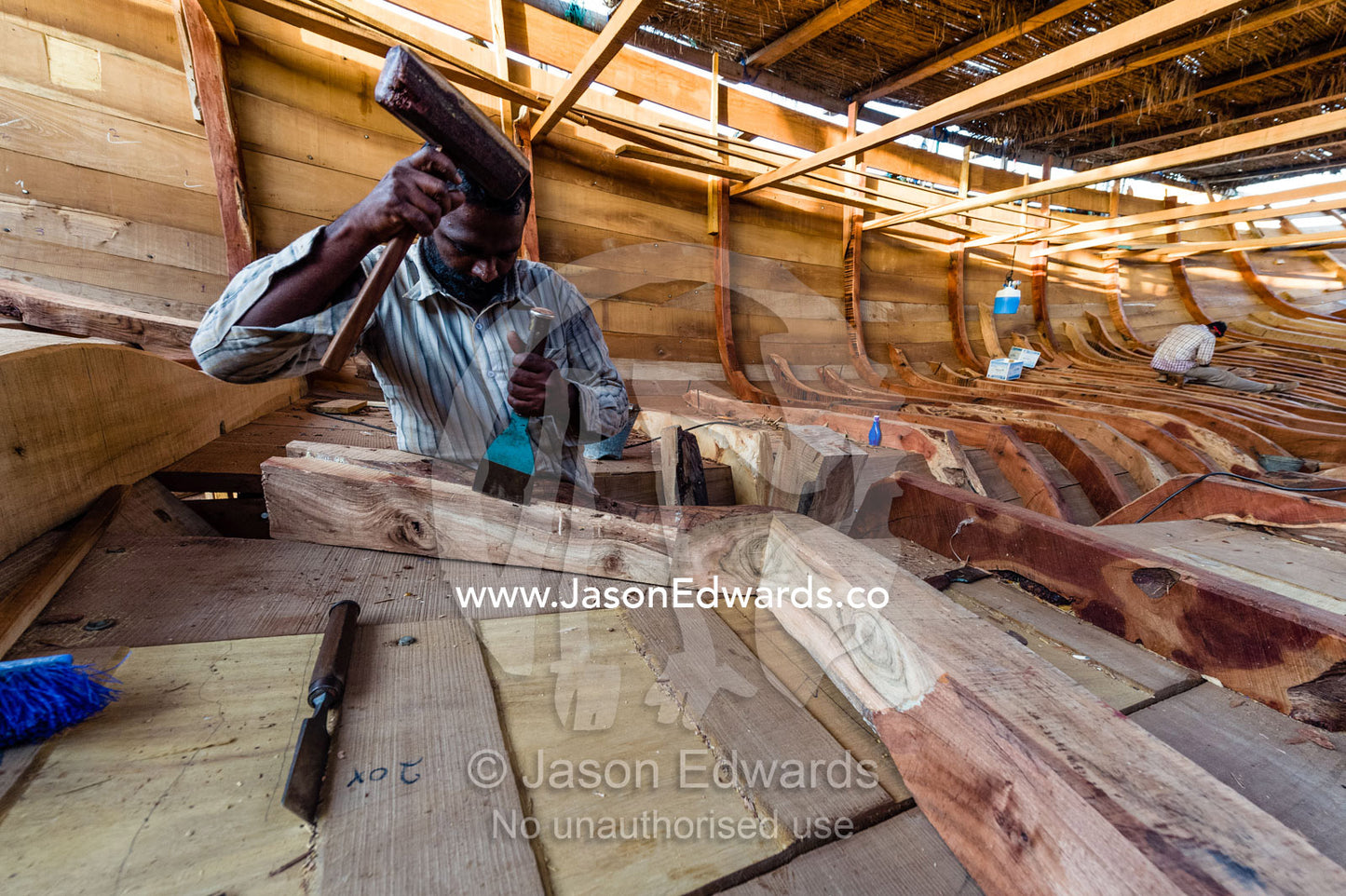 Laborers chisel and shape timber hull ribs during handmade construction of an ancient timber dhow. Sur, Ash Sharqiyah Region, Gulf of Oman, Sultanate of Oman.