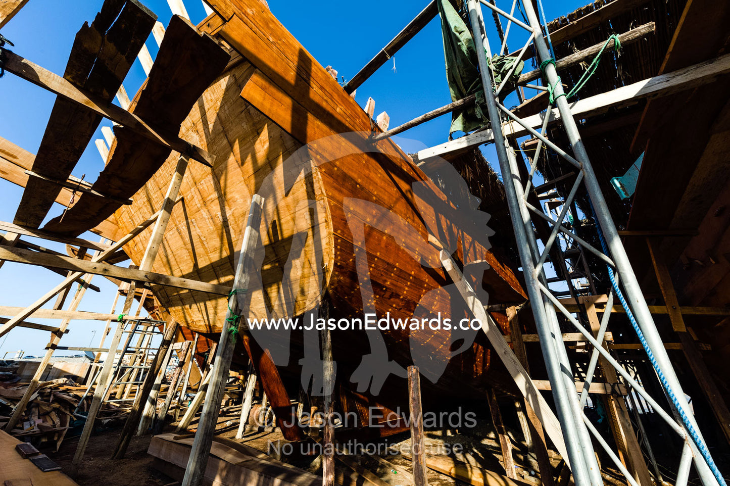 Scaffolding supports the hull during handmade construction of an ancient timber dhow in a ship building yard. Sur, Ash Sharqiyah Region, Gulf of Oman, Sultanate of Oman.