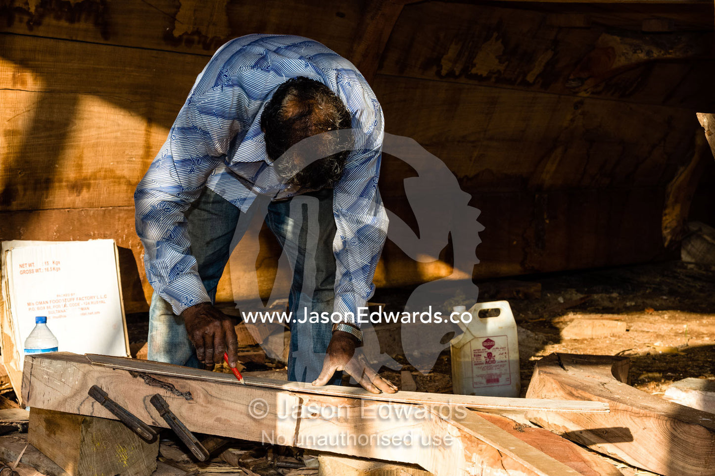 Laborers measures and shape timber hull ribs during handmade construction of an ancient timber dhow. Sur, Ash Sharqiyah Region, Gulf of Oman, Sultanate of Oman.
