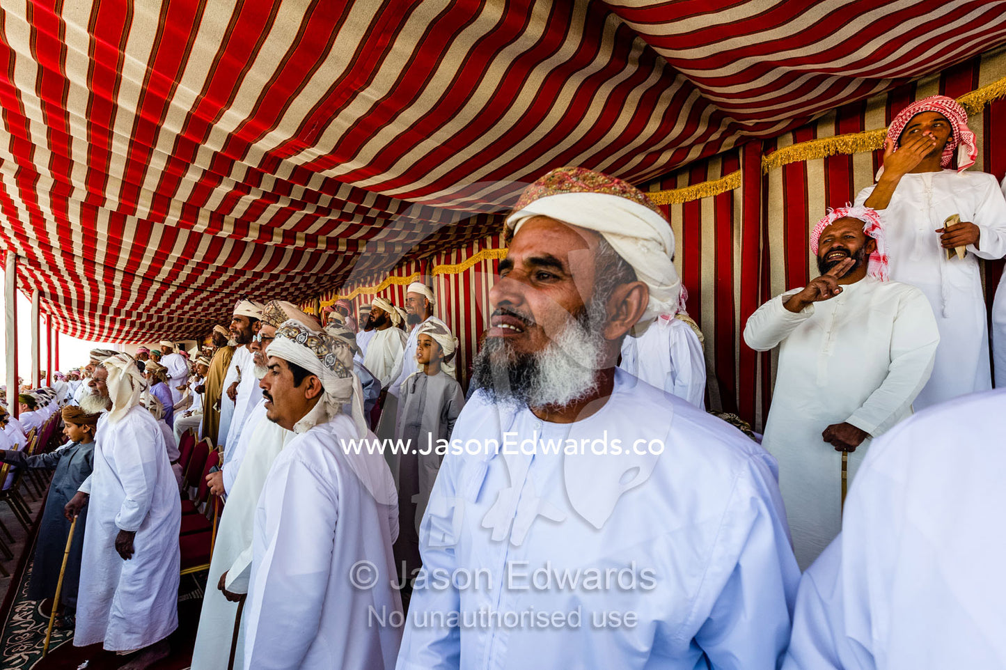 Muslim elders watch camel races from the shade of a striped tented pavilion. Bidiya, Sharqiya Region, Sultanate of Oman.