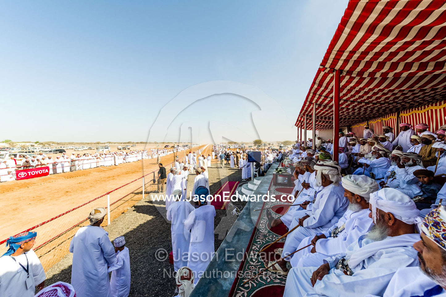 Muslim elders watch camel races from the shade of a striped tented pavilion. Bidiya, Sharqiya Region, Sultanate of Oman.