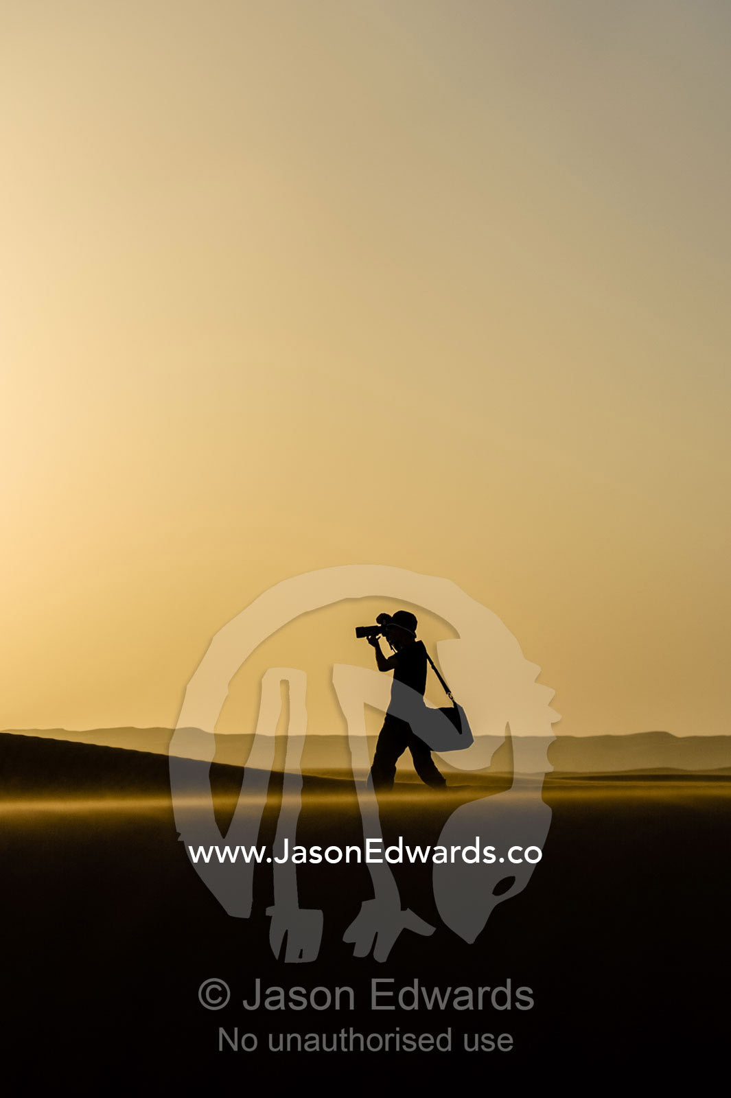 The silhouette of a photographer taking photos on a sand dune at sunset. Wahiba Sands, Ramlat al-Wahiba, Sharqiya Sands, Sultanate of Oman.