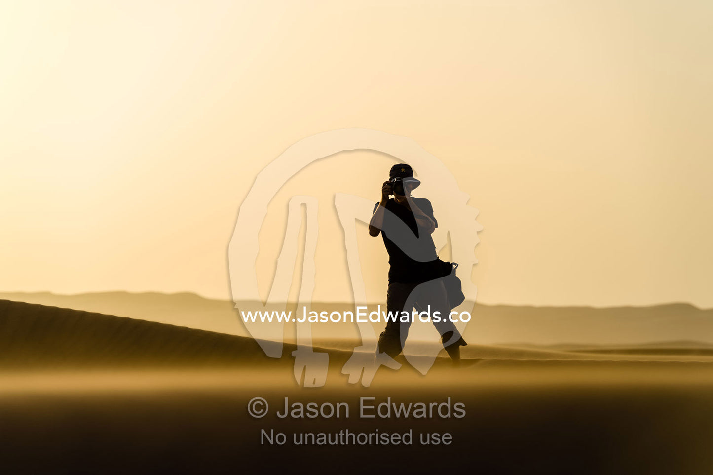 The silhouette of a photographer taking photos on a sand dune at sunset. Wahiba Sands, Ramlat al-Wahiba, Sharqiya Sands, Sultanate of Oman.