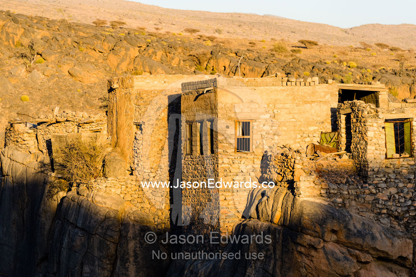 Sunset touches the walls of an ancient mud brick village on a desert gorge mountainside. Misfat Al Abryeen, Al Hajar Mountains, Al Hamra, Ad Dakhiliyah Region, Sultanate of Oman.