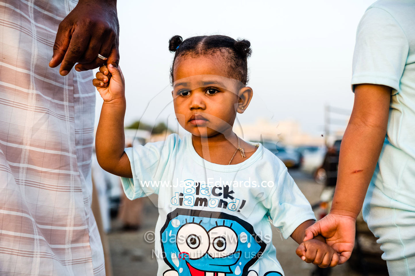 Young sisters watch a traditional bull fight with their father. Al Sharadi, Seeb, Muscat, Sultanate of Oman.