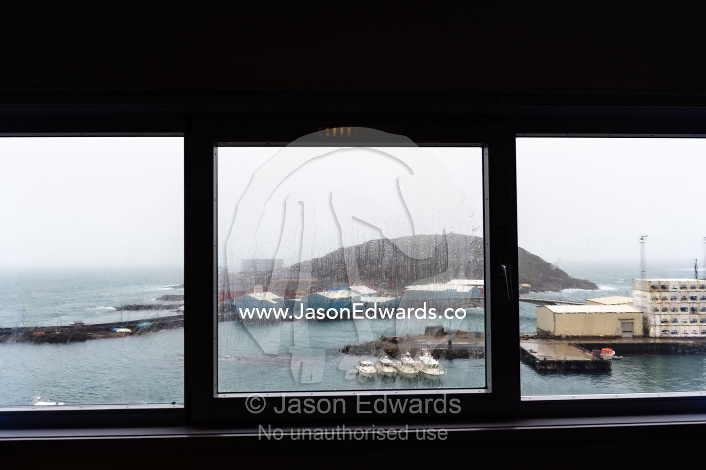 Looking through insulated windows on a rainy afternoon over a fishing port. Maniitsoq, Sukkertoppen, Qeqqata Municipality, Greenland.