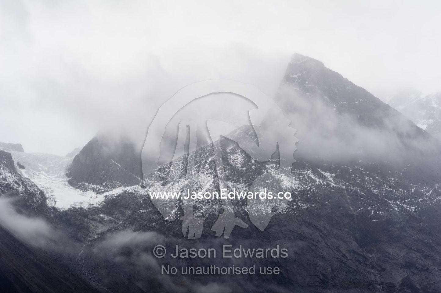Cloud and mist shroud jagged and rugged mountain peaks during a rain storm in a fiord. Fjord of Eternity, Maniitsoq, Sukkertoppen, Qeqqata Municipality, Greenland.